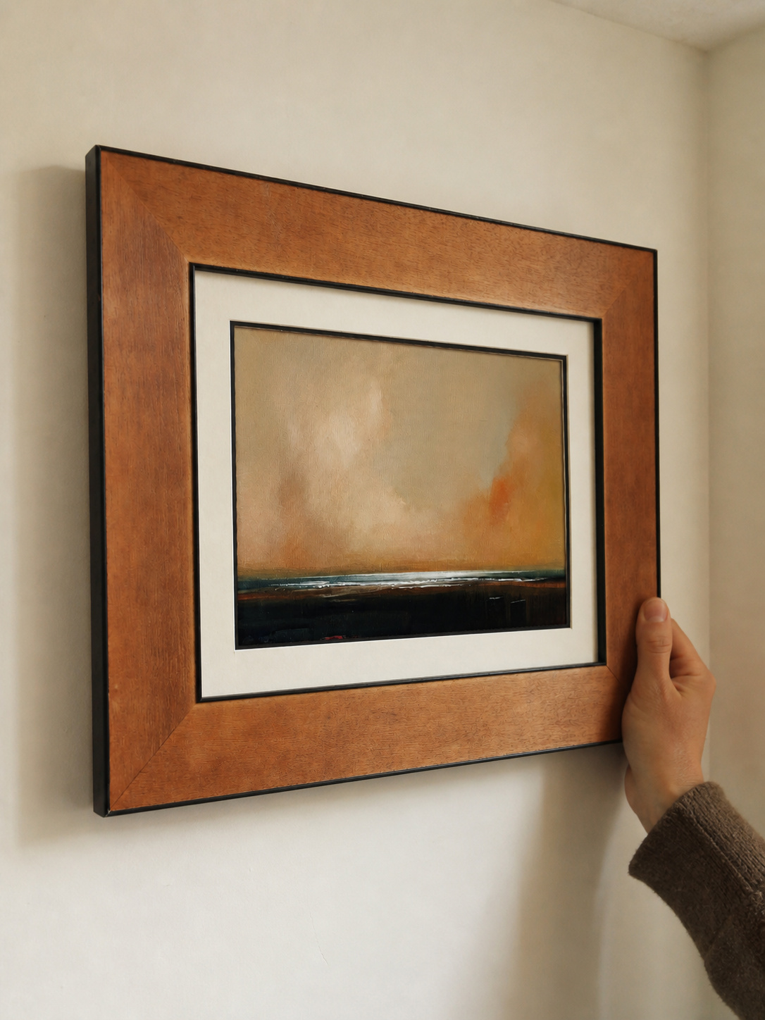 MOOJI ART warm amber landscape framed wall art with a hand steadying the warm brown frame during installation